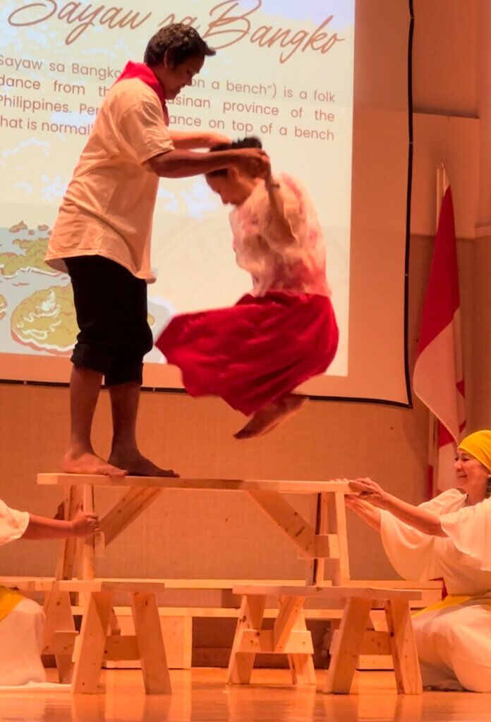 A man holds a woman by her hands as she jumps on top of a wooden bench